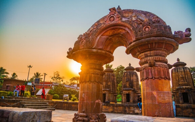 Ancient stone temple with a carved archway and smaller shrines in the background during sunset